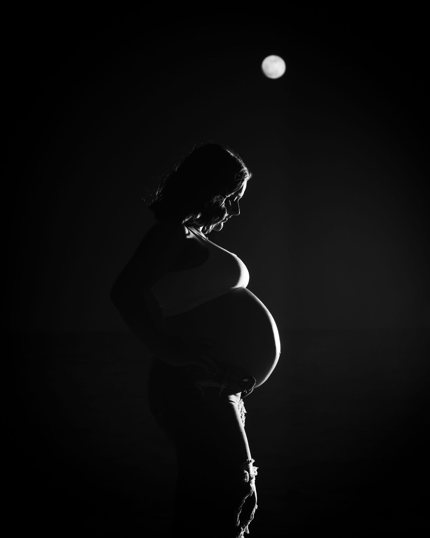 Black-and-white maternity silhouette beneath the moon